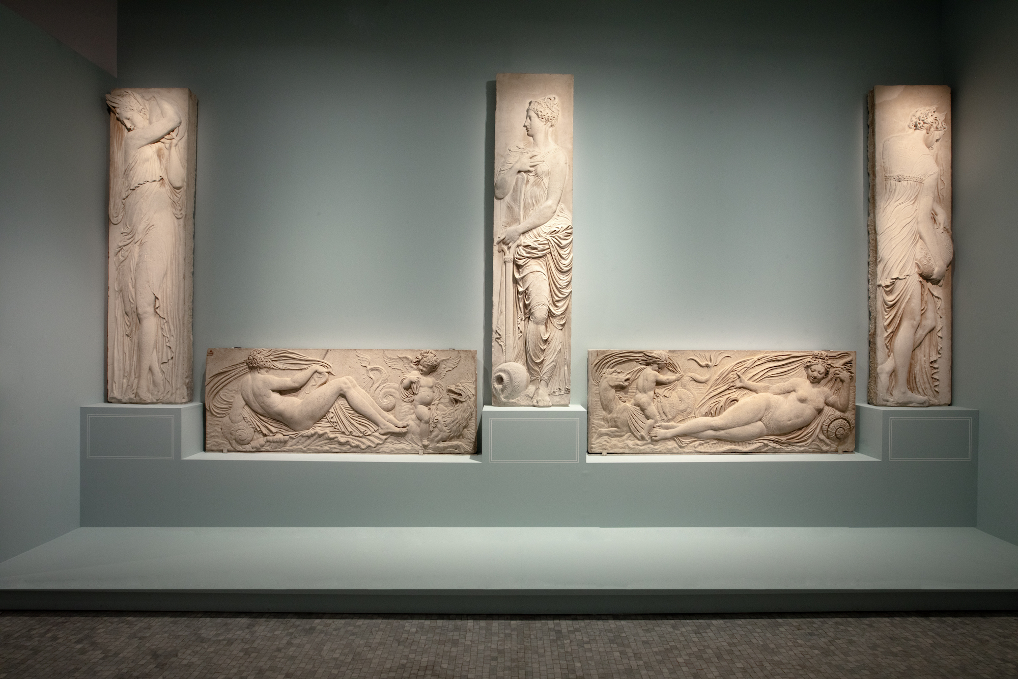 Dans le parcours d’exposition, trois nymphes de la fontaine présentées aux côtés de deux reliefs du soubassement conservés au Louvre © Paris Musées – G. Deblonde