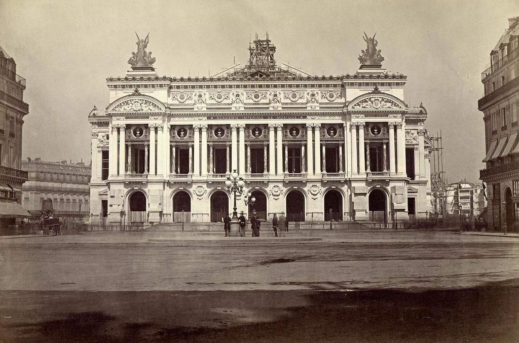 Delmaet et Durandelle, Chantier de construction de l’Opéra : dévoilement de la façade principale, 15 août 1867. Photographie positive sur papier albuminé montée sur carton, 26 x 38 cm. Paris, BnF, Bibliothèque-musée de l’Opéra. La photographie a été retouchée pour ajouter les groupes de Gumery sur l’attique de la façade : ils étaient absents en 1867.
