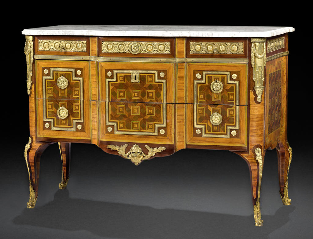 Commode en bois de rose et marqueterie géométrique, la façade à double ressaut ouvrant à cinq tiroirs sur trois rangs, à décor de quartefeuilles dans des carrés sur un fond de losanges dans des encadrements de laiton doré à rosaces dans les décrochements, le dessus de marbre blanc reposant sur des montants arrondis prolongés par des pieds cambrés, ornementation de bronzes dorés à frise d’entrelacs, chutes tablier et sabots ; numéro du Garde-Meuble de la Couronne inscrit à l’encre : du N°2613 /2 (biffé) et numéro d’inventaire du château de Marly : M. N°97, sous le marbre : du N° 2613/2 (à l’encre) et lettre B incisée. Estampille de Daniel Deloose, ébéniste reçu maître en 1767 et JME. Époque Louis XV, 1771. 90,5 x 128,5 x 56,5 cm. Estimé : 40 000/60 000 €.