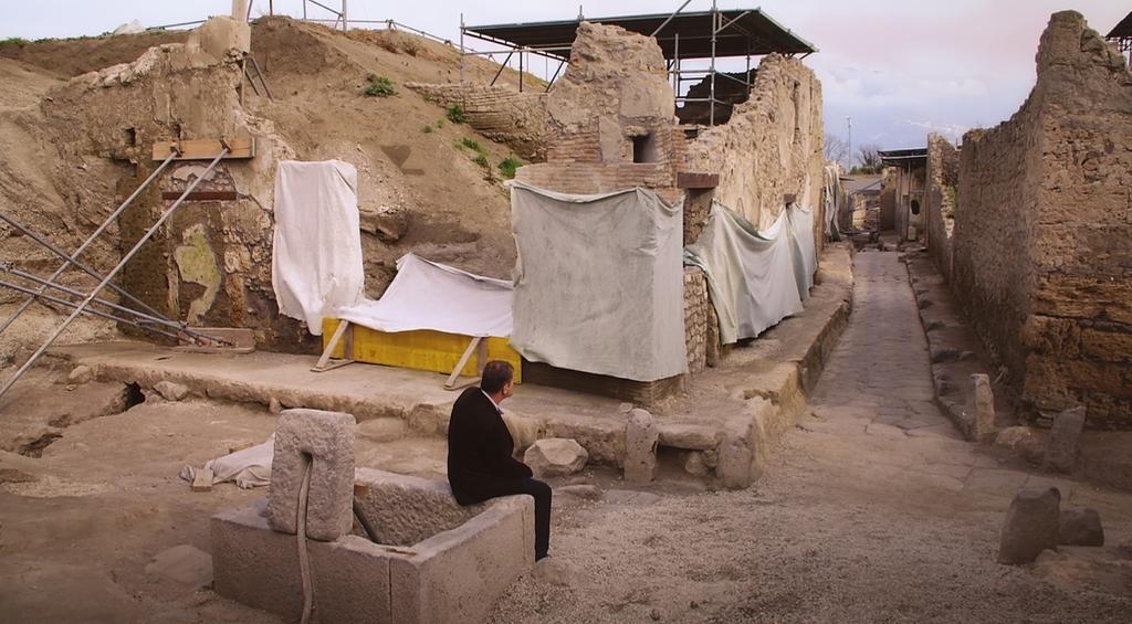Vue de la rue aux balcons après les fouilles. M. Osanna est assis sur la petite fontaine. Pompéi, Parc archéologique de Pompéi.