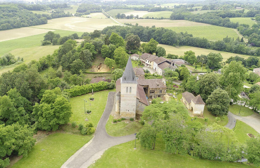 Vue générale du site vers l’ouest : au fond la motte aujourd’hui arborée ; au premier plan, de gauche à droite, l’ancien cimetière, l’église paroissiale et le logis en pan de bois.