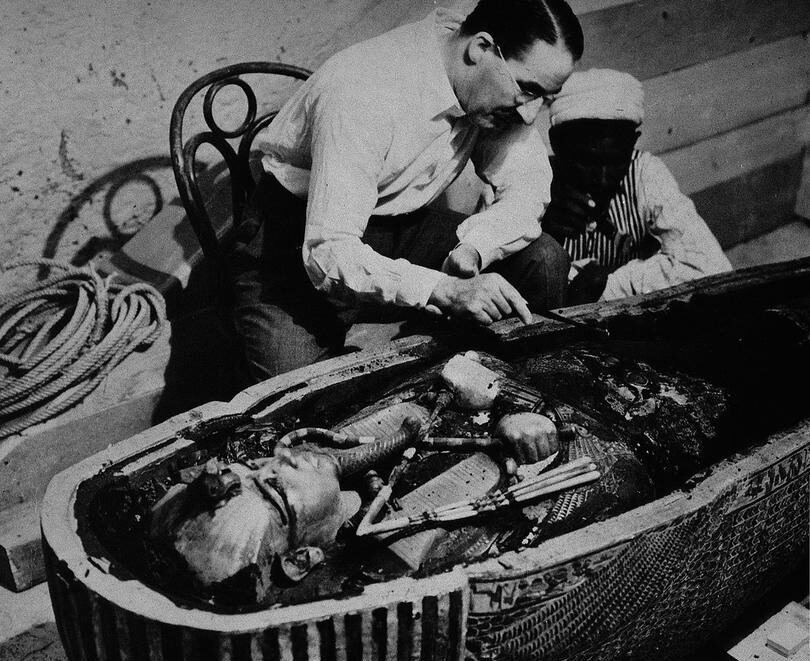 Howard Carter et un ouvrier égyptien examinant le troisième cercueil de Toutânkhamon en or massif dans le second cercueil et cassant les fragments solidifiés de résine noire. Octobre 1925.