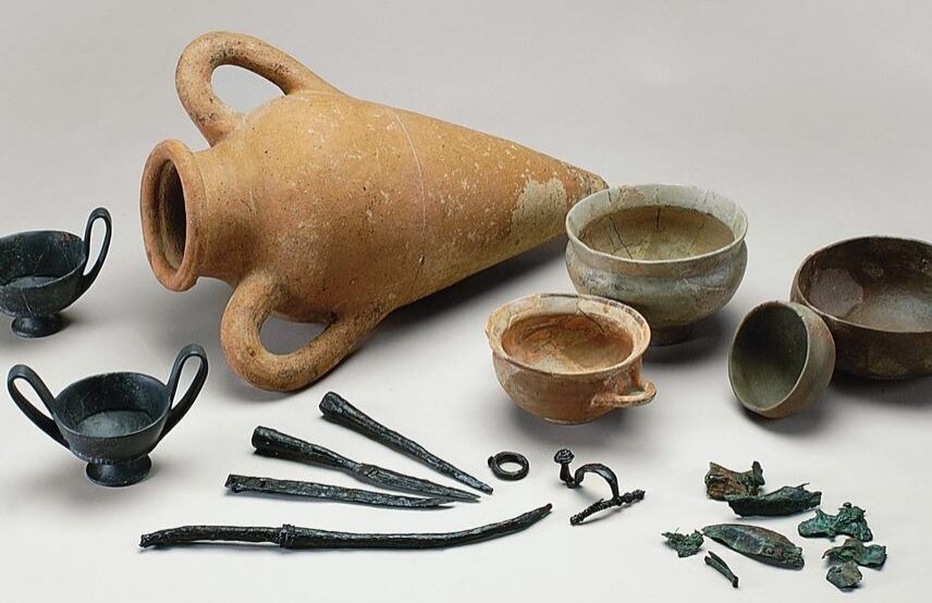 Mobilier funéraire de la tombe Saint-Antoine de Castelnau-de-Guers près d’Agde (Hérault), première moitié du VIᵉ siècle avant notre ère : fibule et armes indigènes, vases étrusques (amphore de transport, canthares en bucchero nero et coupe étrusco-corinthienne) et locaux (coupe en céramique grise et bol non tourné).