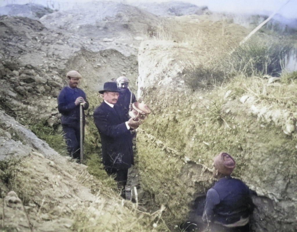 Félix Mouret tenant un vase (cinéraire) découvert dans une des tranchées creusées par ses ouvriers dans la nécropole. Image coloriée des années 1920.