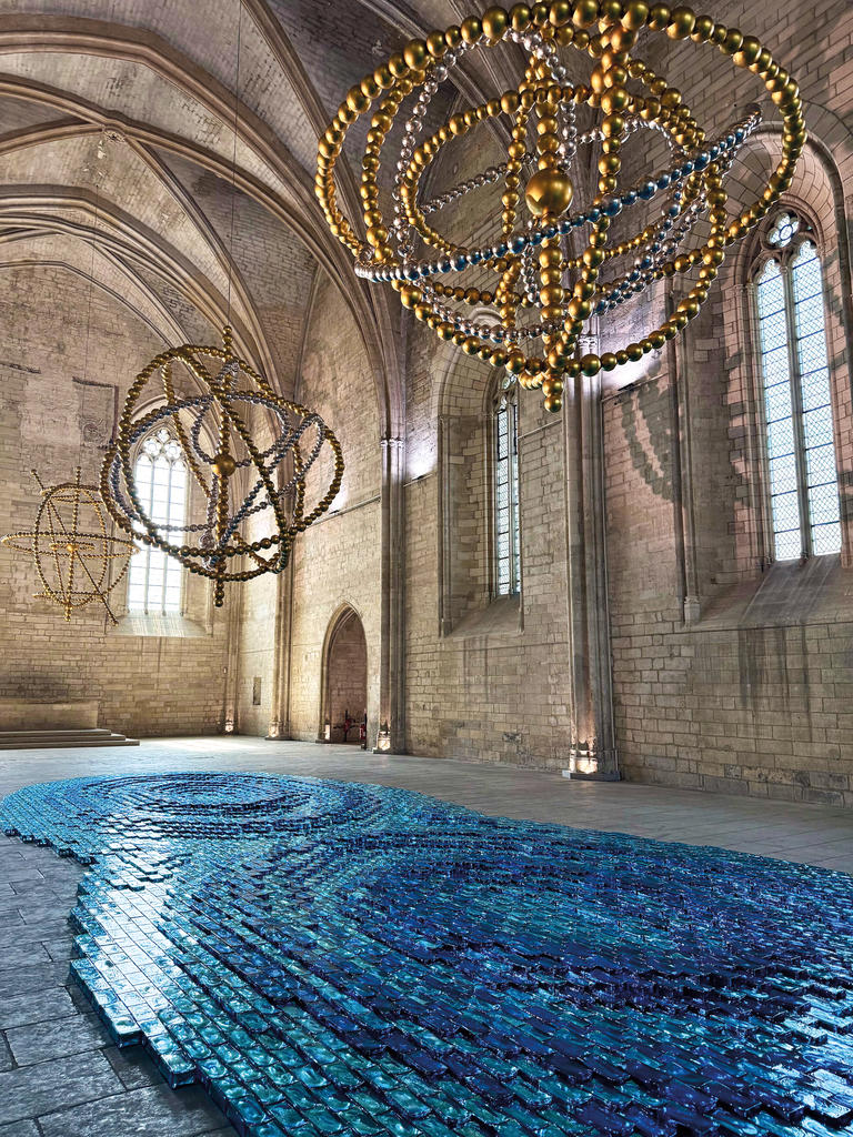 Sous le titre Cosmos, quatre astrolabes géants sont accrochés à la voûte de la Grande Chapelle du palais des Papes, au-dessus de la Rivière bleue, composée de 7 500 briques de verre bleu, 2025.